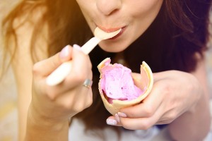 A woman eating bubble gum ice cream from a cone with a spoon